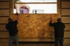 Des ouvriers protègent la vitrine d’un magasin avec des panneaux de bois, vendredi à Paris.