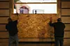 Des ouvriers protègent la vitrine d’un magasin avec des panneaux de bois, vendredi à Paris.